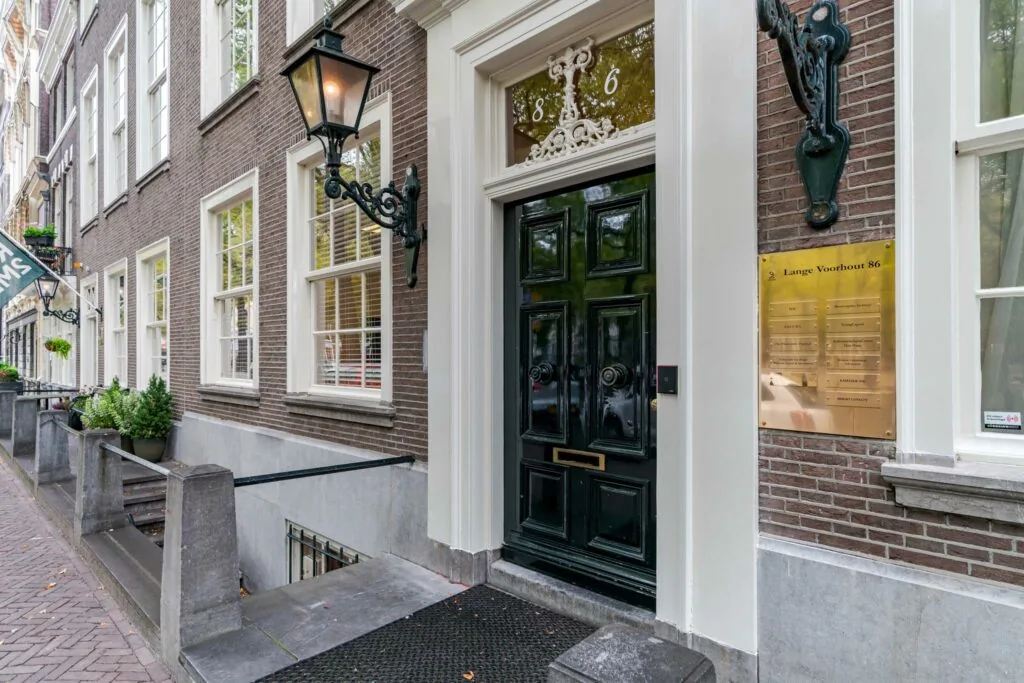 Ingang van een statig pand aan Lange Voorhout 86 met donkere voordeur, gevelverlichting en bedrijfsnaamplaat.